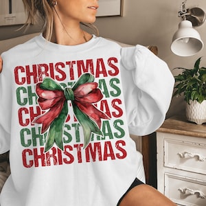 May include: White sweatshirt with the word "CHRISTMAS" in red and green block letters. A watercolor bow in red and green is centered on the front. The sweatshirt has long sleeves.