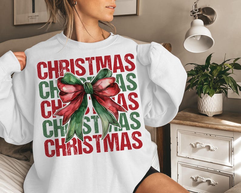 May include: White sweatshirt with the word "CHRISTMAS" in red and green block letters. A watercolor bow in red and green is centered on the front. The sweatshirt has long sleeves.