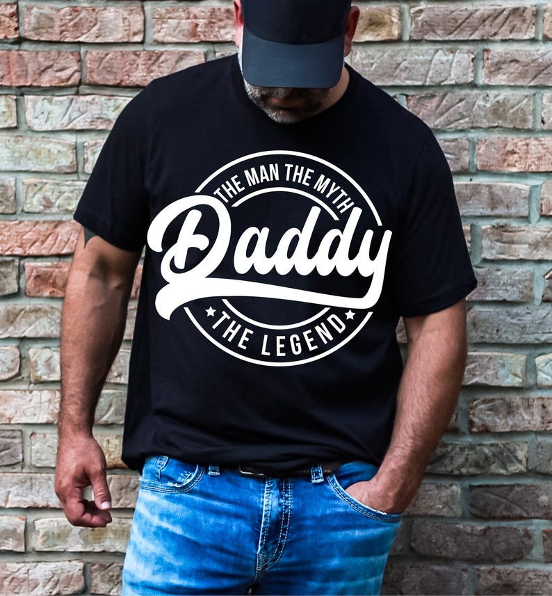 May include: A black t-shirt with a white circle graphic that says "The Man The Myth Daddy The Legend".