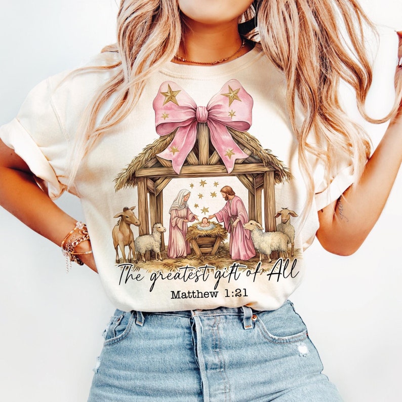 The Greatest Gift of All text design with a nativity scene illustration and pink bow