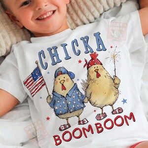 May include: White t-shirt with a patriotic design featuring two cartoon chickens. One chicken holds an American flag, the other a sparkler. The shirt has the words "CHICKA BOOM BOOM" in blue and red.