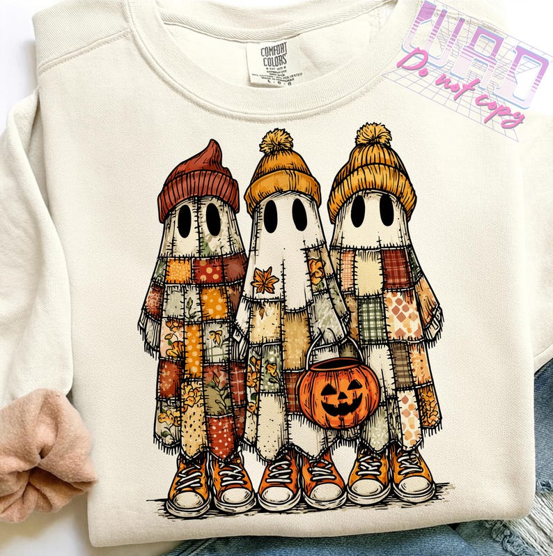 May include: Cream-colored sweatshirt featuring a graphic of three ghost figures in patchwork outfits and orange beanies. The ghosts are wearing orange sneakers and holding a jack-o'-lantern bucket. The sweatshirt has the Comfort Colors brand label.