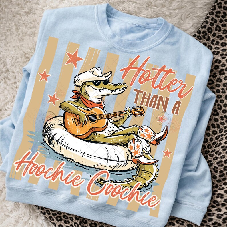 May include: Light blue sweatshirt with a graphic of an alligator wearing a cowboy hat, sunglasses, and boots, playing a guitar while floating on an inner tube. Text reads "Hotter Than A Hoochie Coochie."