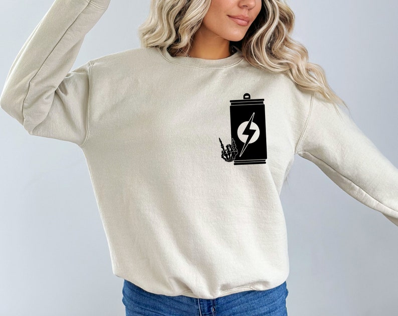 May include: A beige sweatshirt with a black graphic of a can with a lightning bolt and a skeleton hand giving the rock and roll sign.