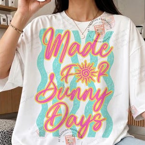 May include: White t-shirt with the text "Made For Sunny Days" in pink and yellow lettering. The design includes a yellow sun graphic and wavy blue lines. A casual, summery style.