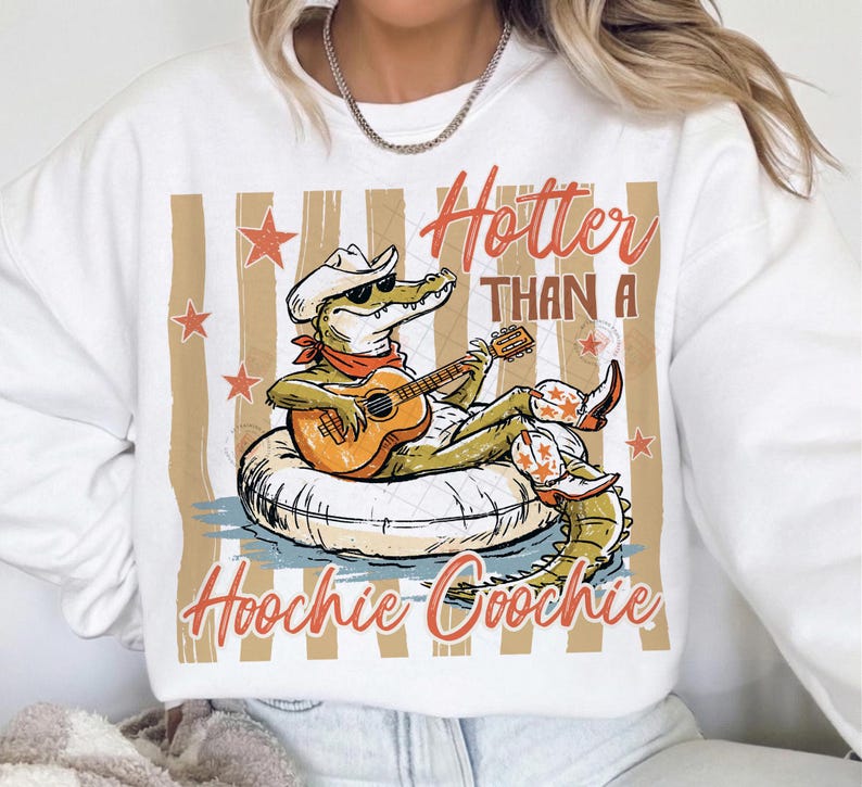 May include: White sweatshirt with a graphic of an alligator wearing a cowboy hat and boots, playing a guitar while floating on an inner tube. The text reads "Hotter Than A Hoochie Coochie" in orange script.