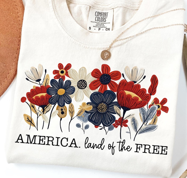 May include: A white t-shirt with a floral design in red, blue, and yellow. The text "AMERICA. land of the FREE" is printed below the flowers.