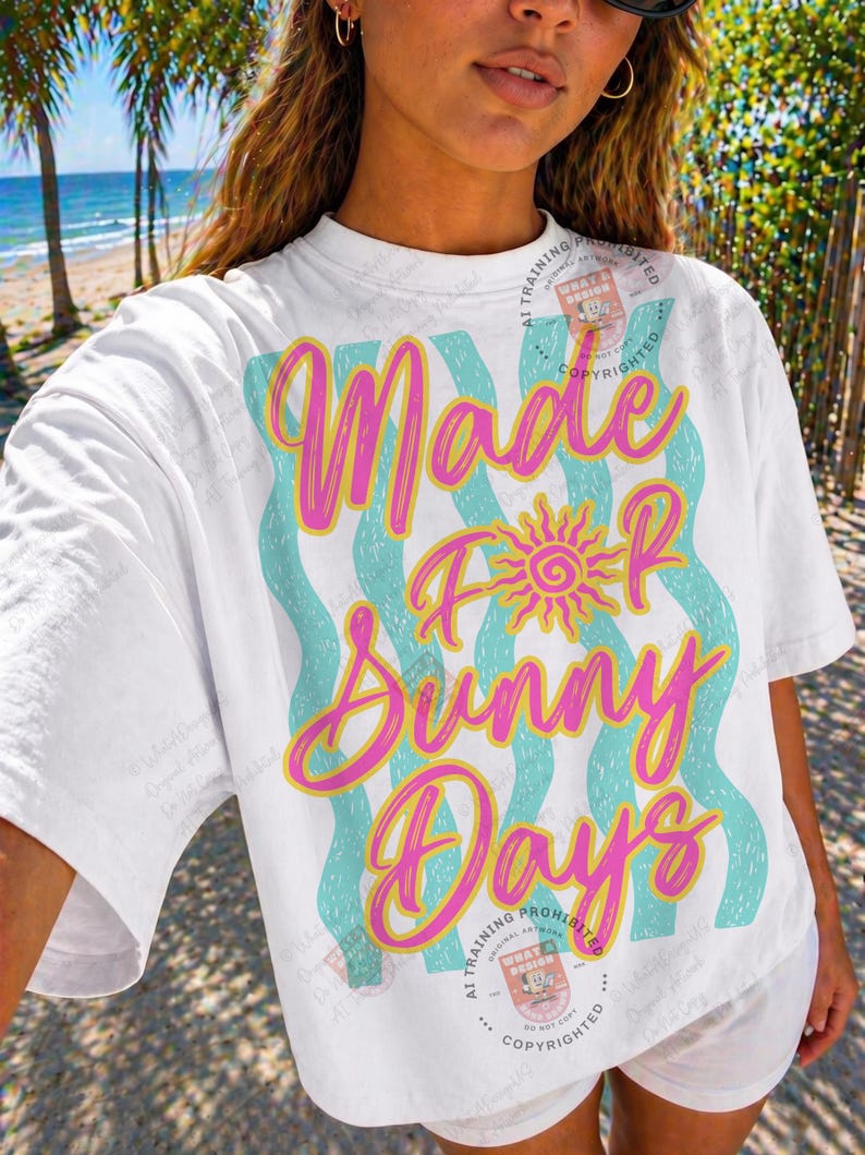 May include: White t-shirt with the text "Made For Sunny Days" in pink and yellow script, with a sun graphic. The text is layered over wavy turquoise stripes. The shirt has short sleeves.