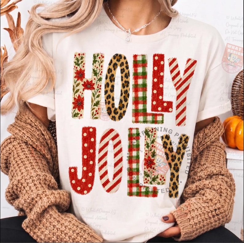 Op de afbeelding: Een cr&egrave;mekleurig t-shirt met de tekst HOLLY JOLLY in grote blokletters. Elke letter heeft een ander patroon, waaronder rode kerststerren, luipaardprint, rood-groene ruiten, rode stippen en rood-witte strepen.