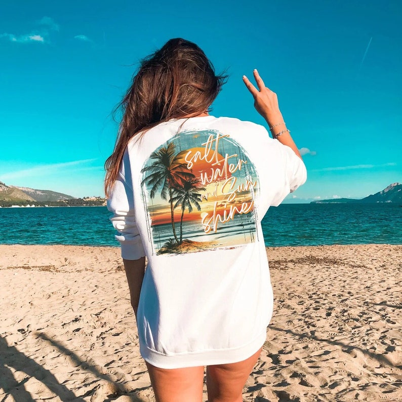 May include: White sweatshirt with a graphic print of a sunset and palm trees. The text "salt water sun shine" is printed on the graphic.