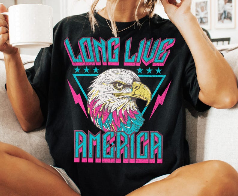 May include: Black t-shirt with a graphic print of an eagle with a pink, blue, and white design. The text "Long Live America" is printed in pink and blue letters.