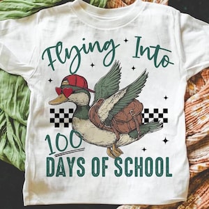 May include: White t-shirt featuring a cartoon duck wearing a red hat and sunglasses, flying with a backpack. The text "Flying Into 100 Days of School" is printed on the shirt.