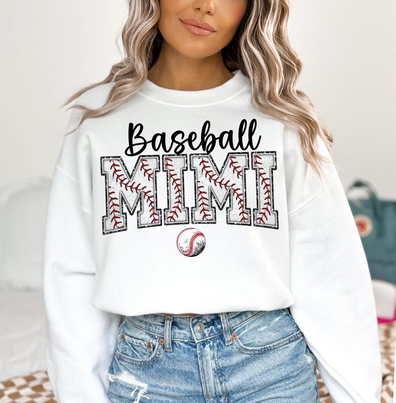 May include: White sweatshirt with the text "Baseball Mimi" in black lettering with a baseball graphic. The text is surrounded by a red and white baseball stitch design.