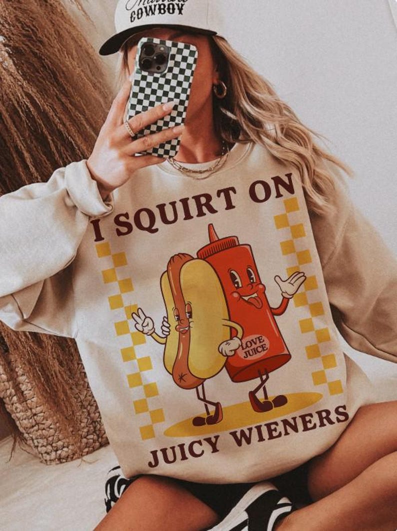 May include: A beige sweatshirt with a graphic of a hot dog and ketchup bottle with the text "I SQUIRT ON JUICY WIENERS" and "LOVE JUICE" printed on it.