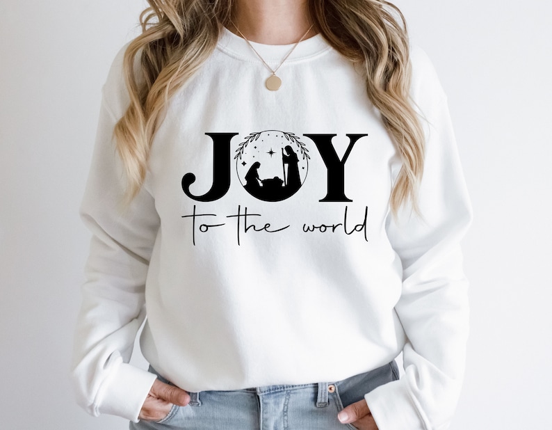 Pu&ograve; includere: Felpa bianca con un design grafico nero che dice "JOY to the world" con una scena della nativit&agrave; all'interno della "O".