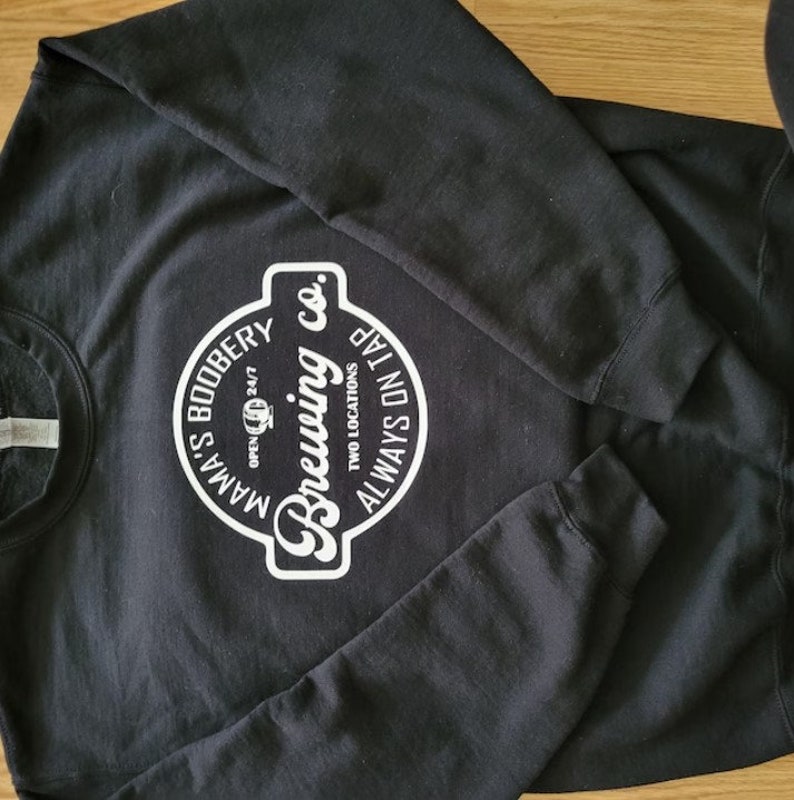 May include: Black sweatshirt with a white logo that says "Mama's Boobery Brewing Co. Two Locations Always On Tap" in a circle.