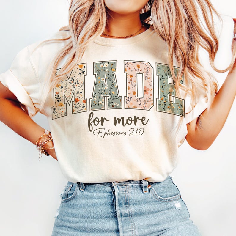 May include: Cream-colored t-shirt with the words "MADE for more" in a floral design. The text "Ephesians 2:10" is below the main text. The shirt is a casual style.
