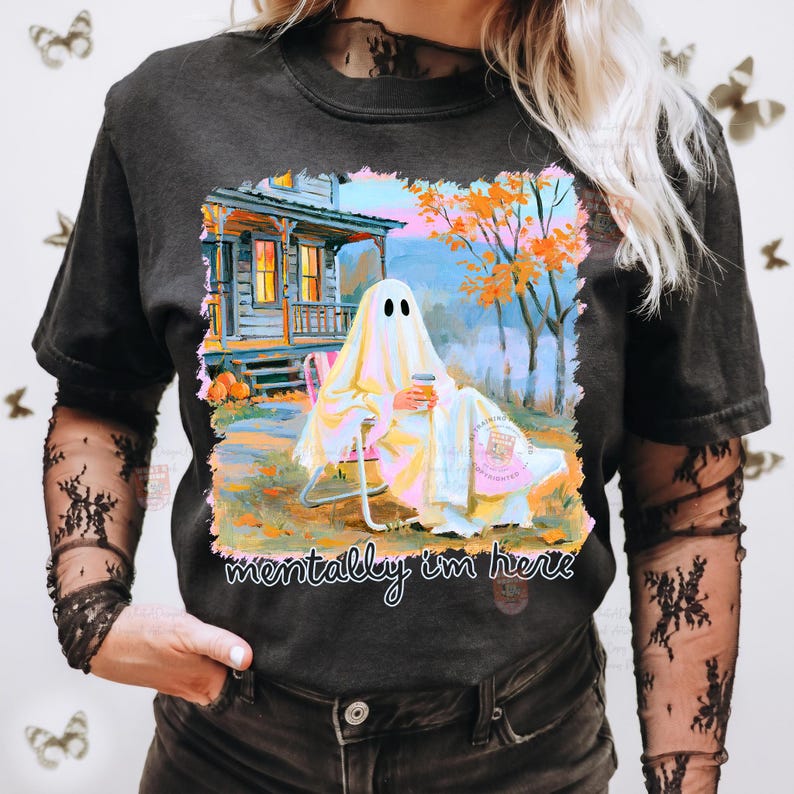 K&ouml;nnte beinhalten: Ein schwarzes T-Shirt mit einem Grafikdruck eines in ein wei&szlig;es Laken geh&uuml;llten Geistes, der in einem Gartenstuhl vor einem Haus mit orangefarbenen Herbstb&auml;umen sitzt und einen Kaffee h&auml;lt. Der Text unter dem Bild lautet, mentally i'm here.