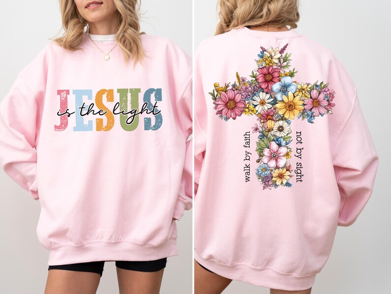 May include: A light pink sweatshirt with the text "Jesus is the light" in colorful letters on the front. The back features a floral cross design with the words "walk by faith, not by sight".