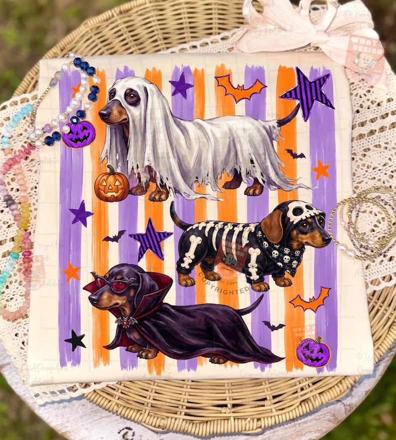 May include: A white t-shirt featuring three dachshunds in Halloween costumes: one as a ghost with a pumpkin, one as a skeleton, and one as a vampire. The background has vertical orange and purple stripes with stars, bats, and jack-o'-lanterns.