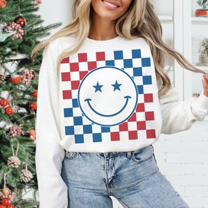 Op de afbeelding: Witte trui met een rood en blauw geruit patroon en een blauwe smiley met sterren voor ogen.