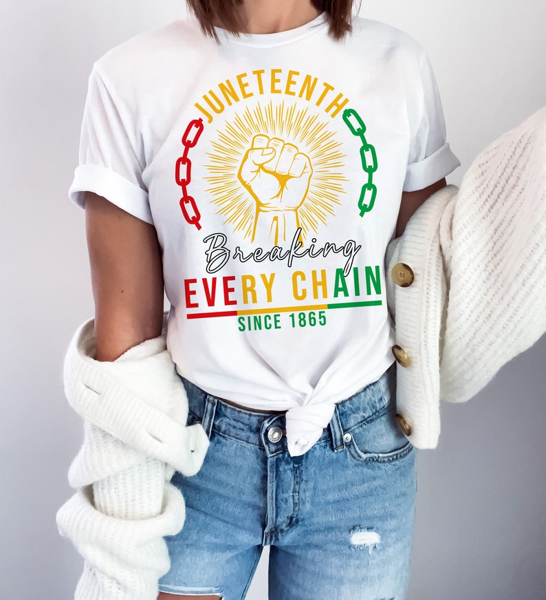 Peut inclure: T-shirt blanc avec un motif graphique repr&eacute;sentant un poing lev&eacute;, des cha&icirc;nes et le texte "Juneteenth Breaking Every Chain Since 1865".