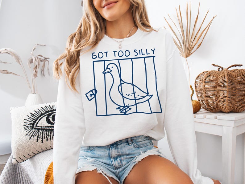 May include: White sweatshirt with a blue graphic of a duck in a cage and the text "GOT TOO SILLY".