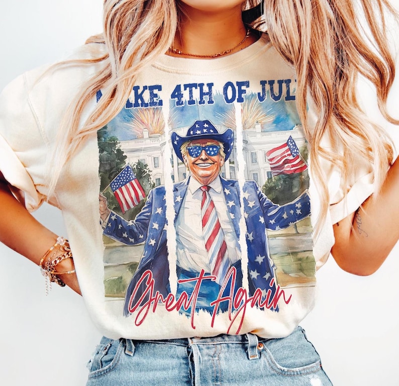 May include: A white t-shirt with a graphic print of a man wearing sunglasses and a cowboy hat, holding American flags. The text "Make 4th of July Great Again" is printed on the shirt.