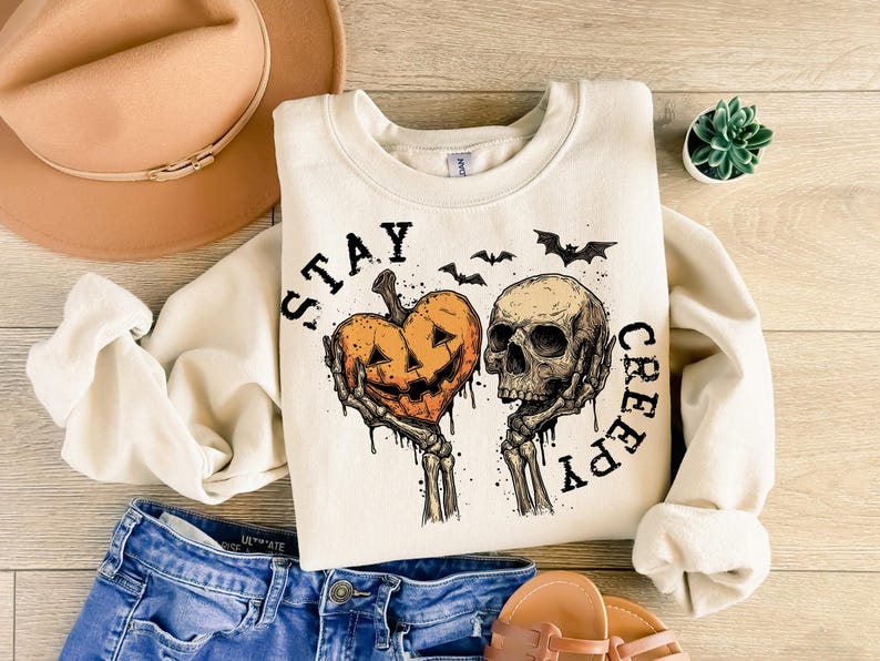 Puede incluir: Sudadera color crema con un gr&aacute;fico tem&aacute;tico de Halloween. El dise&ntilde;o presenta un coraz&oacute;n de calabaza tallada y una calavera sostenida por manos esquel&eacute;ticas, con las palabras "STAY CREEPY" en negro. Tambi&eacute;n se incluyen murci&eacute;lagos.
