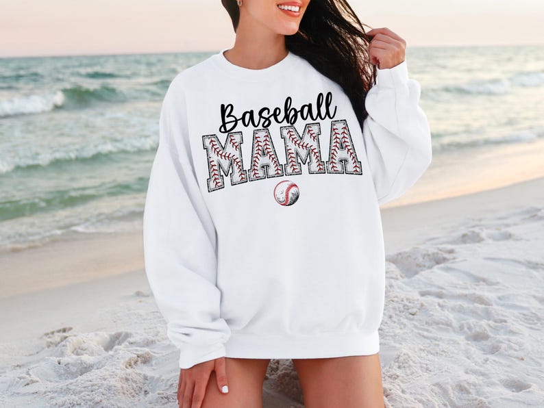 May include: White sweatshirt with the text "Baseball Mama" in black letters with a baseball graphic design. The letters are outlined in red and white stitching.