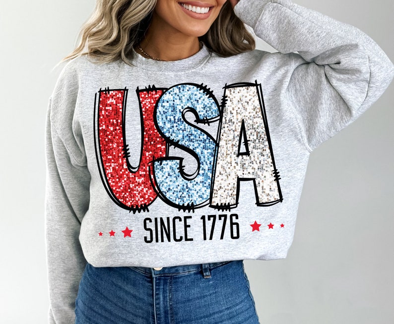 May include: A gray sweatshirt with a glittery red, white, and blue "USA" graphic and the text "Since 1776" with red stars.