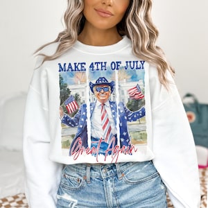 May include: White crewneck sweatshirt with a graphic featuring a man in a cowboy hat and a suit with American flag details. The text "MAKE 4TH OF JULY" and "Great Again" are displayed above and below the image.