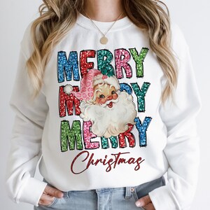 Op de afbeelding: Witte trui met een feestelijk ontwerp met een vintage illustratie van de kerstman en de tekst "Merry Merry Christmas" in kleurrijke glinsterende letters.