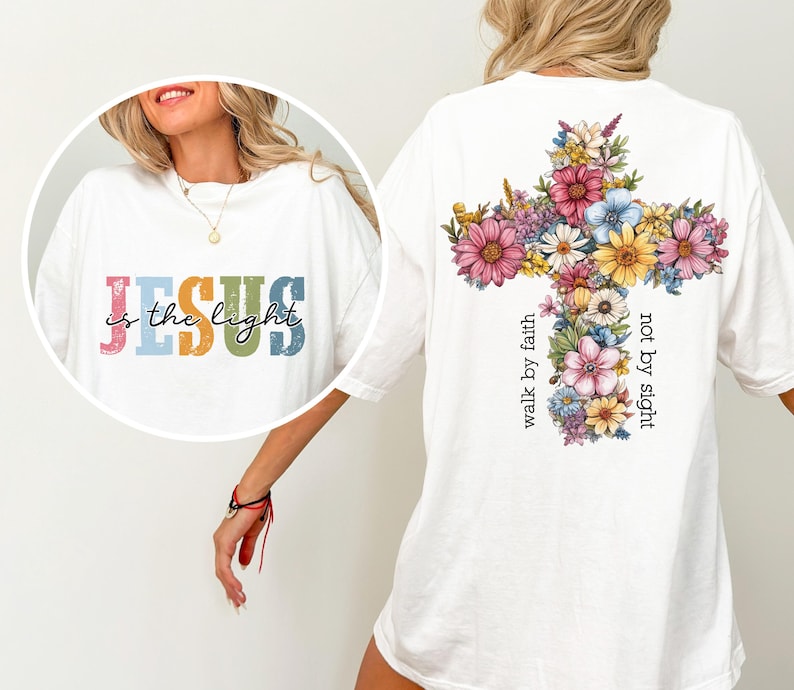 May include: White t-shirt with the text "JESUS is the light" in colorful letters on the front. The back features a floral cross design with the words "walk by faith not by sight".