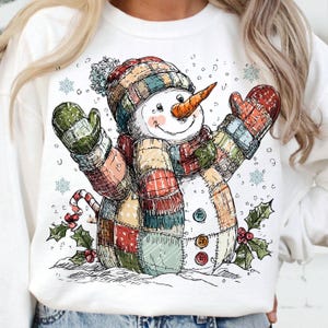 Könnte beinhalten: Weißes Sweatshirt mit einem skurrilen Schneemann-Design. Der Schneemann trägt einen Patchwork-Hut, Schal und Fäustlinge in verschiedenen Farben. Er hat eine Karottennase, Knopfaugen und eine Zuckerstange. Schneeflocken und Stechpalmenzweige vervollständigen den festlichen Look.