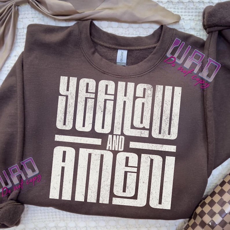 May include: A brown sweatshirt with the words "YEEHAW AND AMEN" printed in a distressed white font. The sweatshirt has a crew neck and long sleeves. The text is centered on the front of the garment.