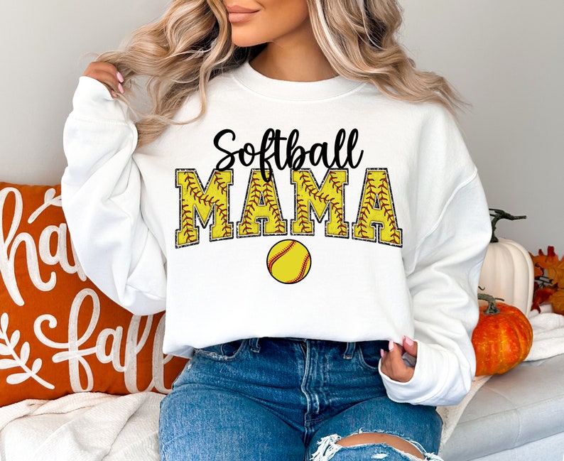May include: White sweatshirt with the text "Softball Mama" in black with a yellow softball graphic. The sweatshirt has long sleeves and a crew neck.