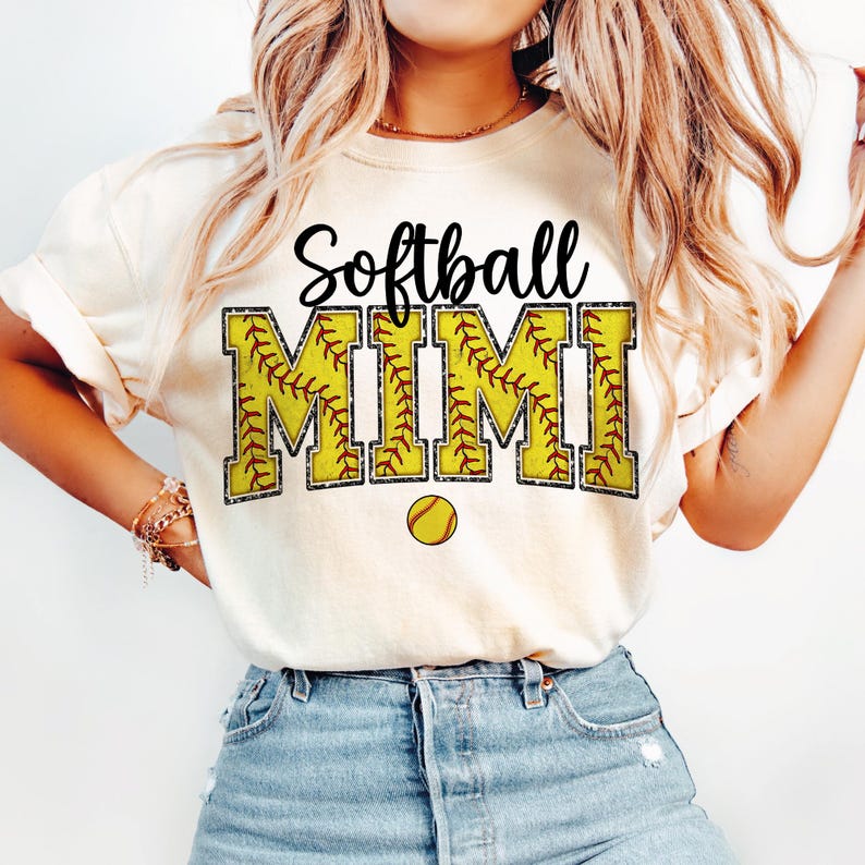 May include: White t-shirt with the text "Softball Mimi" in black and yellow. The text is decorated with a softball pattern.