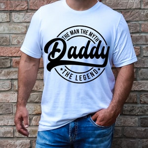 May include: White t-shirt with a black circle graphic that says "The Man The Myth Daddy The Legend".