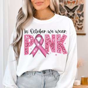 May include: White sweatshirt with long sleeves and a pink glitter design that says "In October we wear PINK" with a pink ribbon.