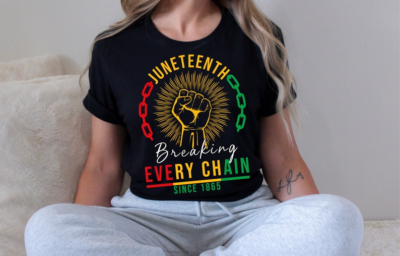 Peut inclure: T-shirt noir avec un motif graphique jaune, rouge et vert. Le motif repr&eacute;sente un poing lev&eacute;, des cha&icirc;nes et le texte "Juneteenth Breaking Every Chain Since 1865".