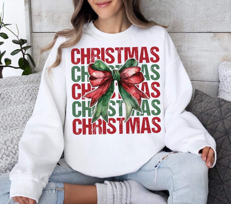 May include: White Christmas sweatshirt featuring a watercolor bow in red and green. The word "CHRISTMAS" is stacked vertically in red and green letters. The sweatshirt is a festive holiday apparel item.