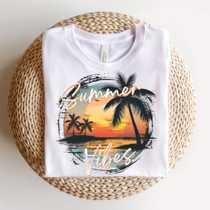 May include: White t-shirt with a graphic design of a sunset with palm trees and the text "Summer Vibes" in a distressed font.