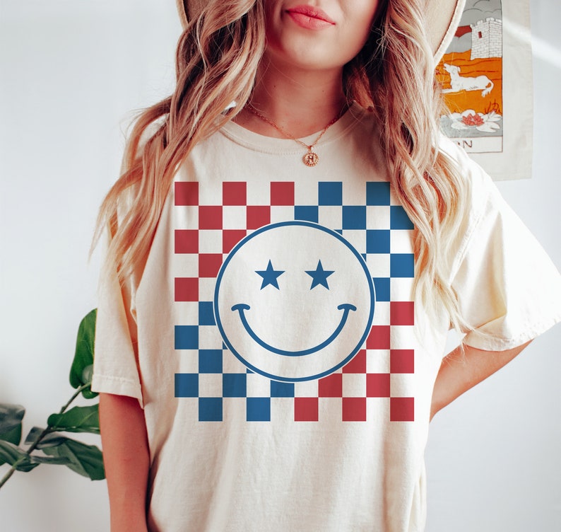 Op de afbeelding: Een wit T-shirt met een blauw-rood geruit patroon en een blauwe smiley met twee sterren als ogen.