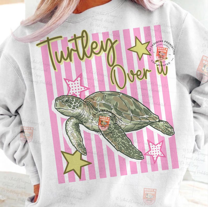 May include: White sweatshirt with a graphic of a sea turtle, stars, and the text "Turtley Over It" in green. The background features pink and white stripes. The turtle is green and brown.