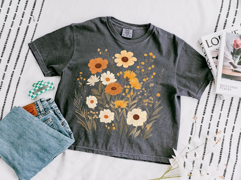 May include: A dark gray t-shirt with a floral print featuring yellow, orange, and white flowers. The flowers are arranged in a bouquet-like design.