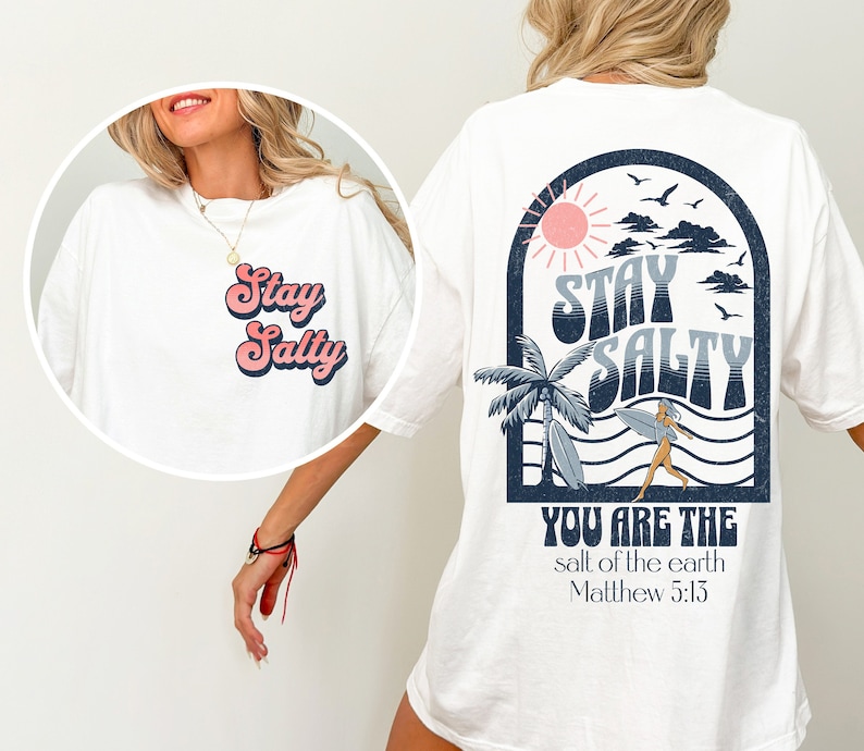 May include: White t-shirt with a retro-style graphic of a surfer girl and the text "Stay Salty" in a blue and pink arch. Below the graphic is the text "You are the salt of the earth Matthew 5:13".