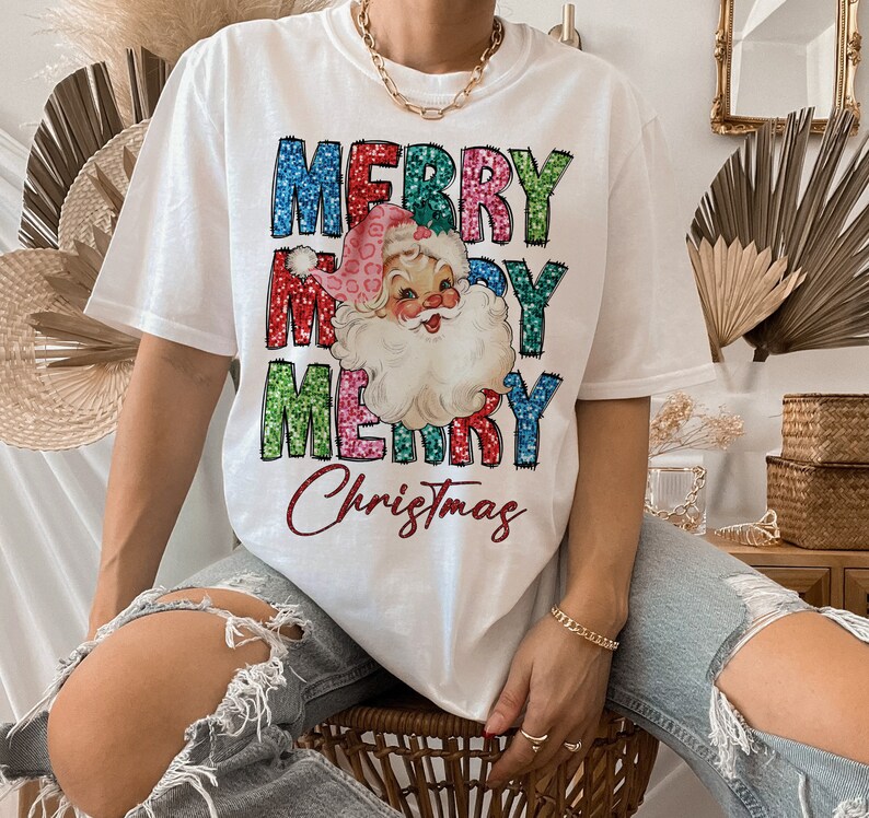 Op de afbeelding: Wit T-shirt met een kleurrijk glitterend "Merry Christmas" ontwerp met een vintage illustratie van de kerstman.
