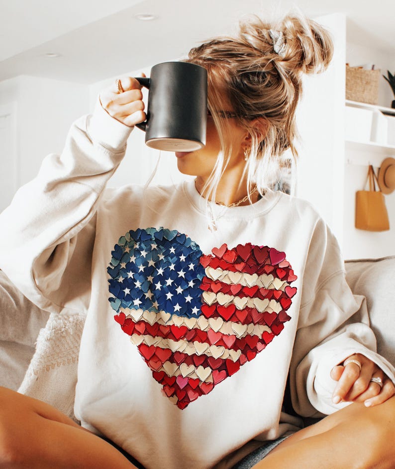May include: White sweatshirt with a red, white, and blue heart-shaped American flag design. The flag is made of small hearts.