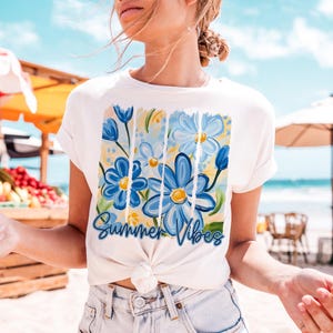 May include: White t-shirt with a blue and yellow floral design and the text "Summer Vibes".
